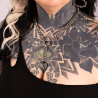 Silberne Herz-Choker-Kette mit Tattoo-Hintergrund Silberne Choker-Kette mit herzförmigem Anhänger auf tätowierter Haut